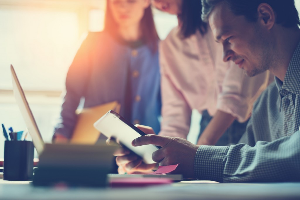 No escritório, diversas pessoas discutem a saúde da empresa, olhando relatórios no computador e no tablet
