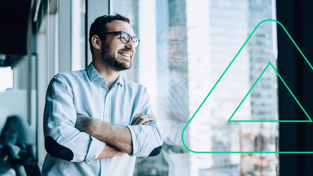 Empresário posando encostado na janela do seu escritório, sorrindo contente com o seu sucesso