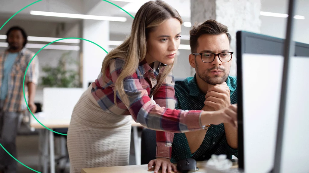 Duas pessoas no escritório da empresa, analisando informações no computador e discutindo sobre o melhor plano de marketing