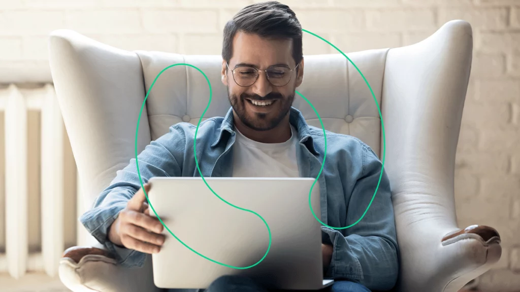 Homem sentado na poltrona em sua casa com o notebook no colo, representando o trabalho remoto de casa