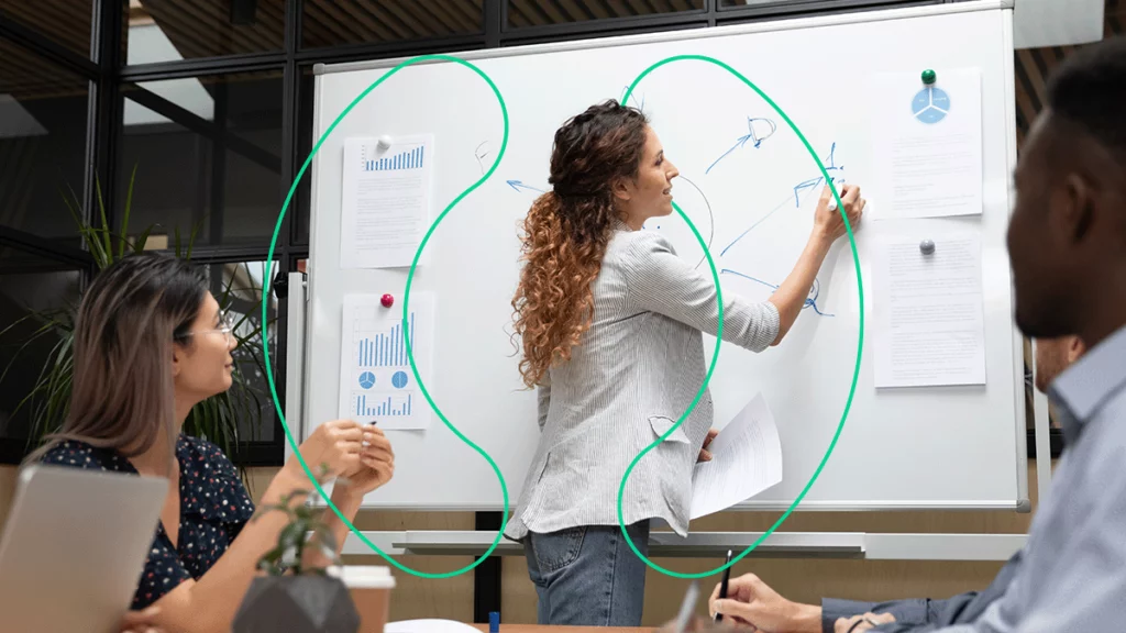 Mulher explicando para um grupo de pessoas como montar um e-commerce, usando um quadro-branco repleto de informações, relatórios e desenhos