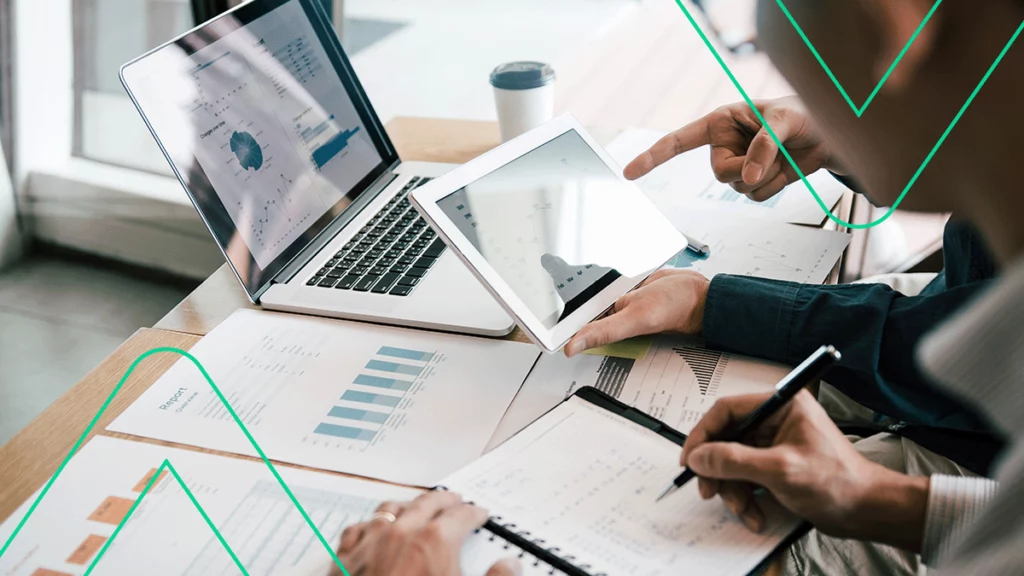 Pessoas analisando vários relatórios em papel, no computador e no tablet, tentando identificar qual é a melhor plataforma de e-commerce