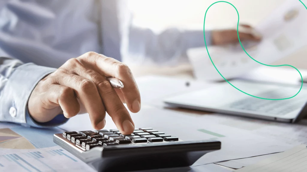 Empreendedor com um papel e caneta na mão usando uma calculadora para calcular o valor do imposto da nota fiscal