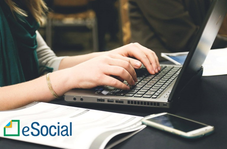 Mulher digitando em um laptop, no escritório de uma empresa; no canto da foto aparece o logotipo do eSocial