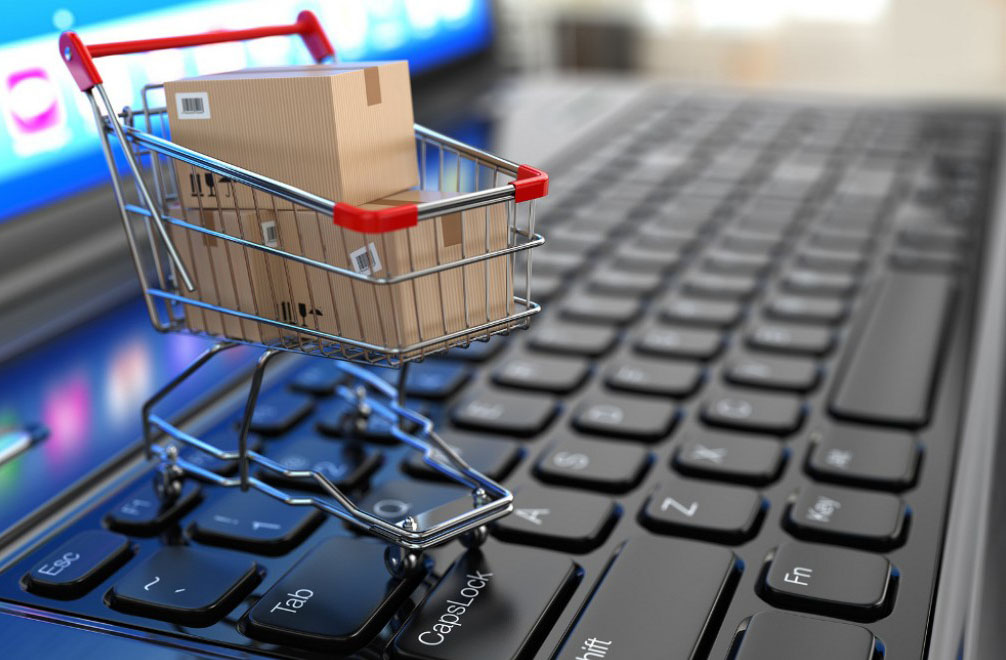Miniatura de um carrinho de supermercado com caixas dentro, posicionado em cima de um laptop aberto