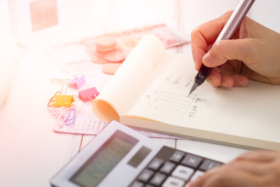 Em um caderninho, empreendora faz anotações e cálculo das contas em uma calculadora