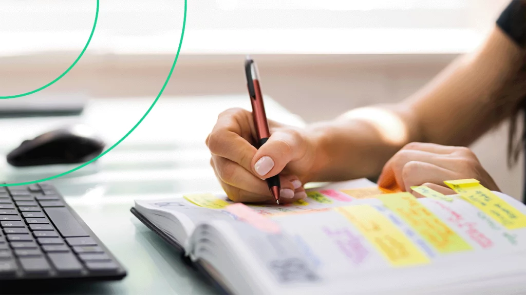 Close-up de uma pessoa escrevendo em uma agenda cheia de anotações e notas adesivas coloridas