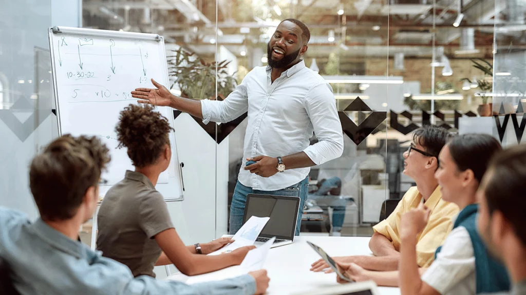 Em uma sala de reuniões, homem usa um quadro branco para explicar para um grupo de pessoas sobre gestão de compra