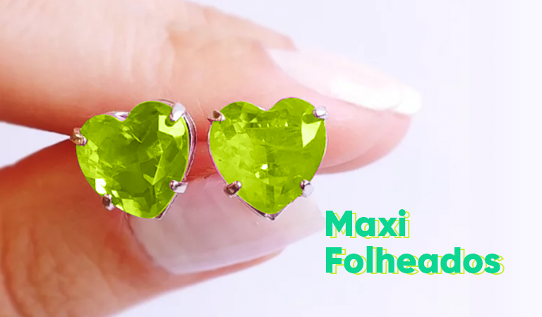 Close-up de dedos segurando um par de anéis em formato de coração, na cor verde; ao lado, aparecem as palavras "Maxi Folheados"