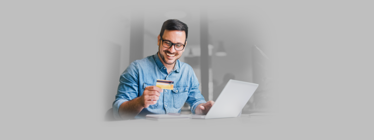 Homem sorri enquanto segura seu cartão de crédito na mão, alegre com as compras que está fazendo no Mercado Livre