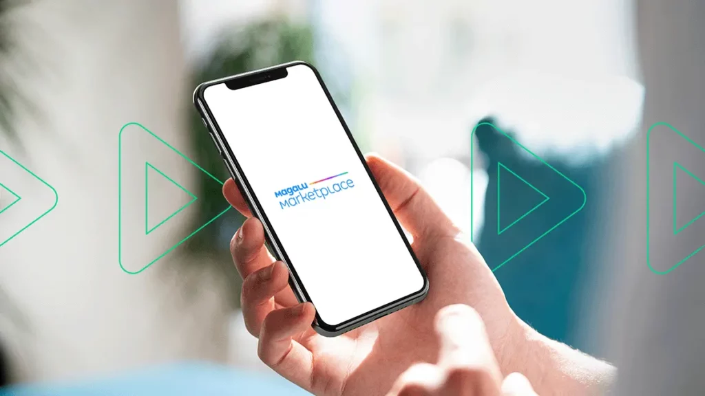 Close-up de uma pessoa segurando um celular com o logotipo do Magalu Marketplace na tela