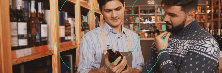 Em um comércio de bebidas, vendedor mostra garrafa de vinho para cliente