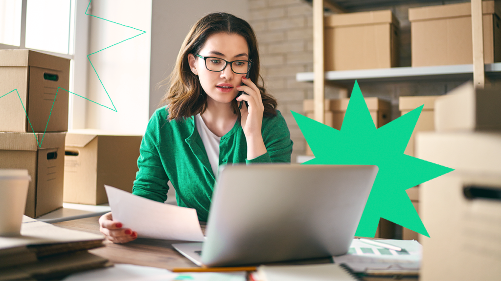 Empreendedora falando no celular enquanto confere documentos na sua mão e no seu computador, tentando entender sobre as mudanças na Tabela NCM 2022 e TIPI 2022